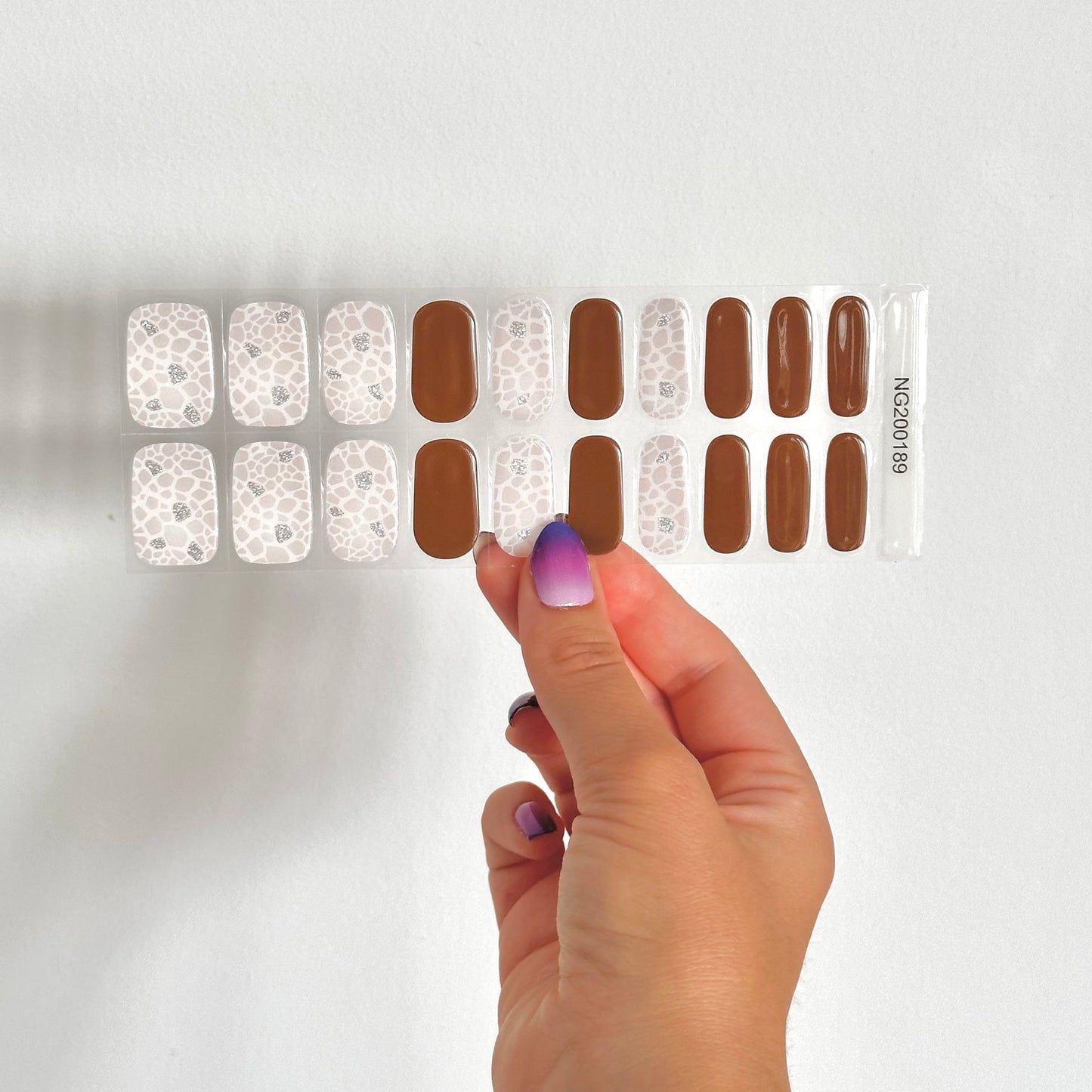 Gellakstickers met op sommige nagels effen bruin en op andere nagels witte panterprint, afgewerkt met subtiele zilveren glitter.