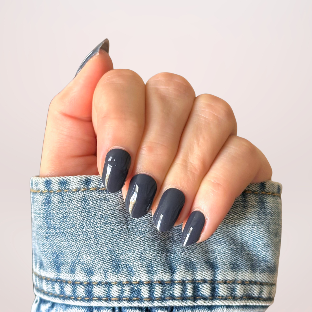Close-up van een hand met donkerblauwe, effen gellakstickers op de nagels, die een diepe en elegante kleur uitstralen met een mooie professionele glans door de top coat