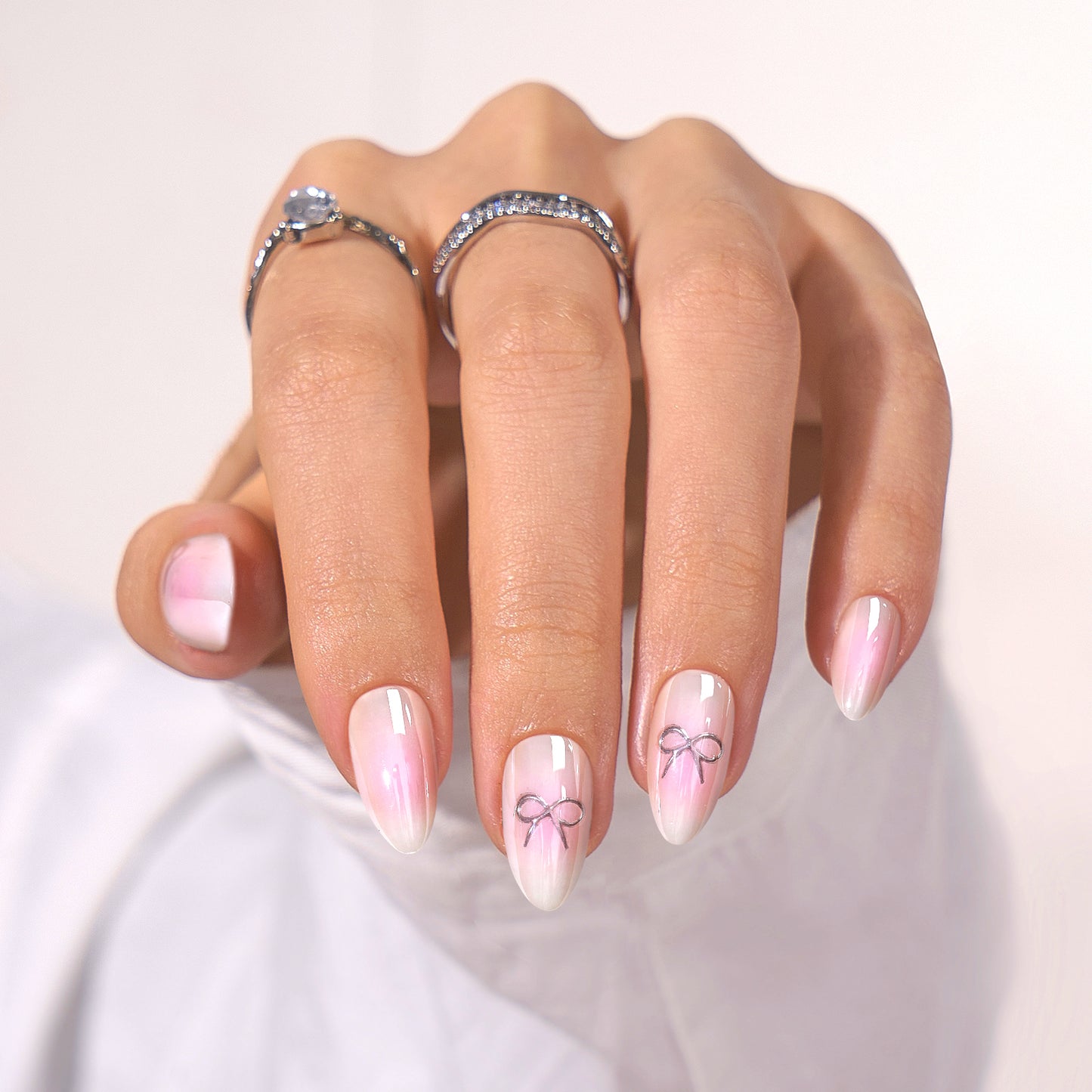 Romantische, schattige roze-witte basis met op sommige nagels een zilveren sierlijke strik als detail.
