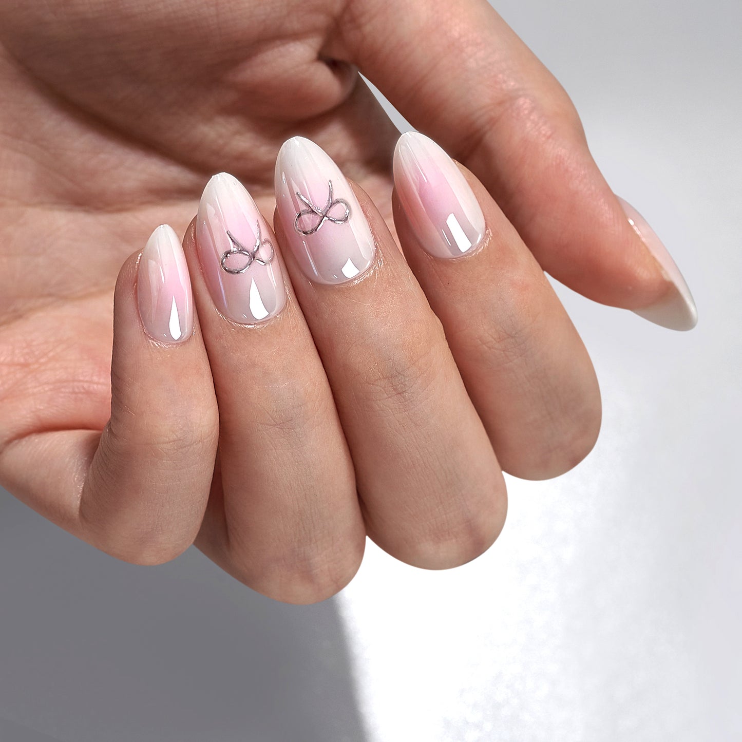 Romantische, schattige roze-witte basis met op sommige nagels een zilveren sierlijke strik als detail.