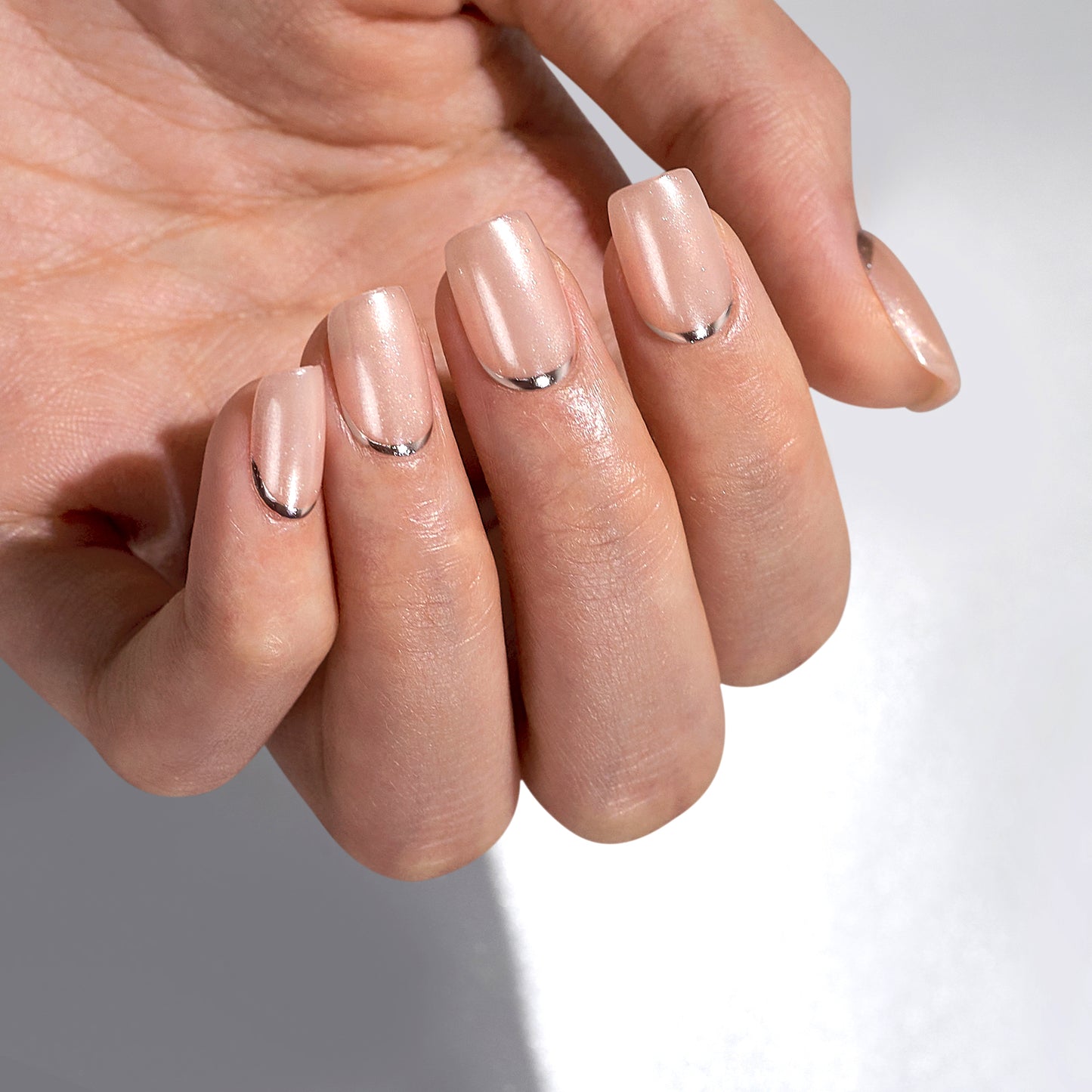 Press on plaknagels in een korte square vorm. Een nude champagne kleurige basis met een matte shimmer afwerking. Onderaan bij de nagelriem een zilveren lijn.