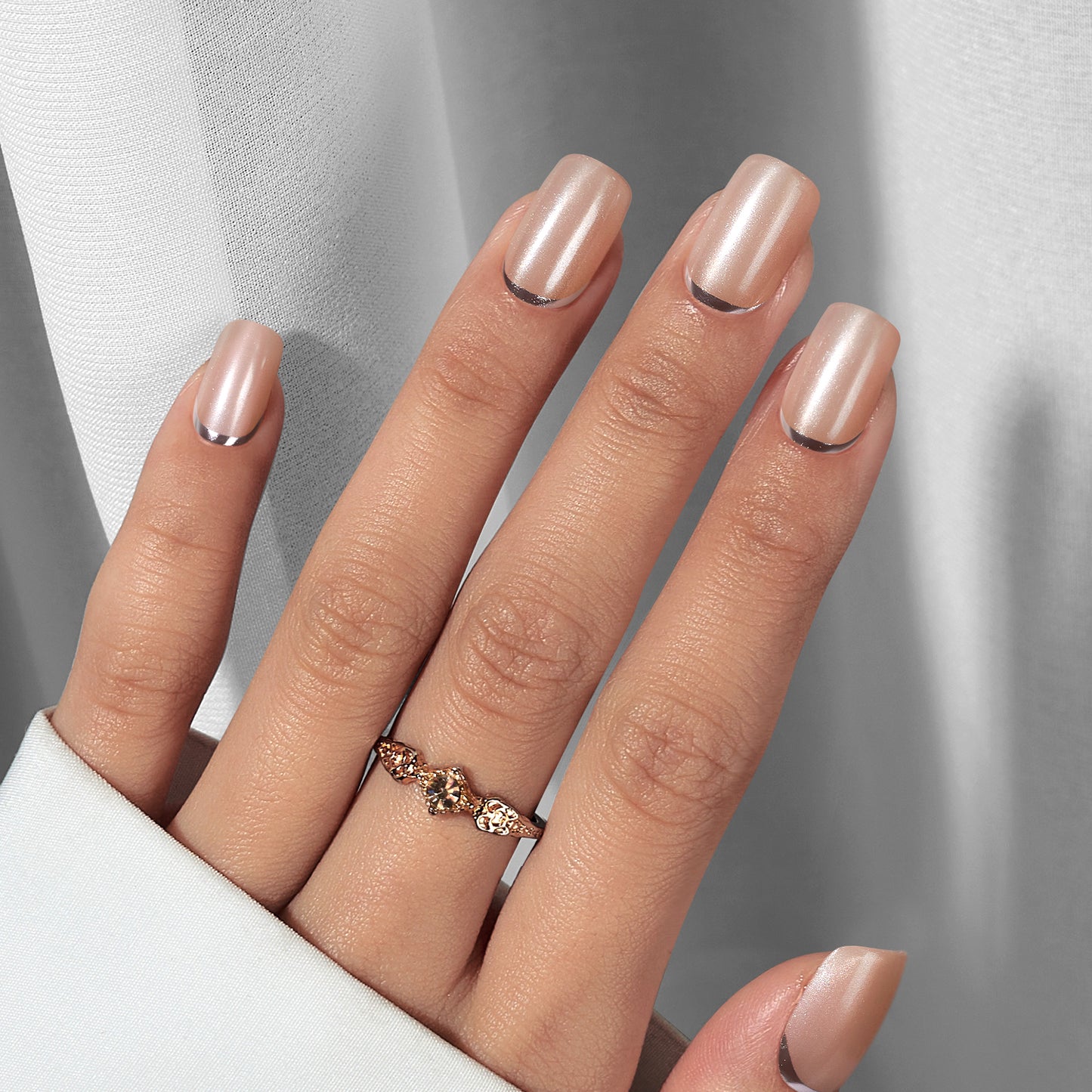 Press on plaknagels in een korte square vorm. Een nude champagne kleurige basis met een matte shimmer afwerking. Onderaan bij de nagelriem een zilveren lijn.
