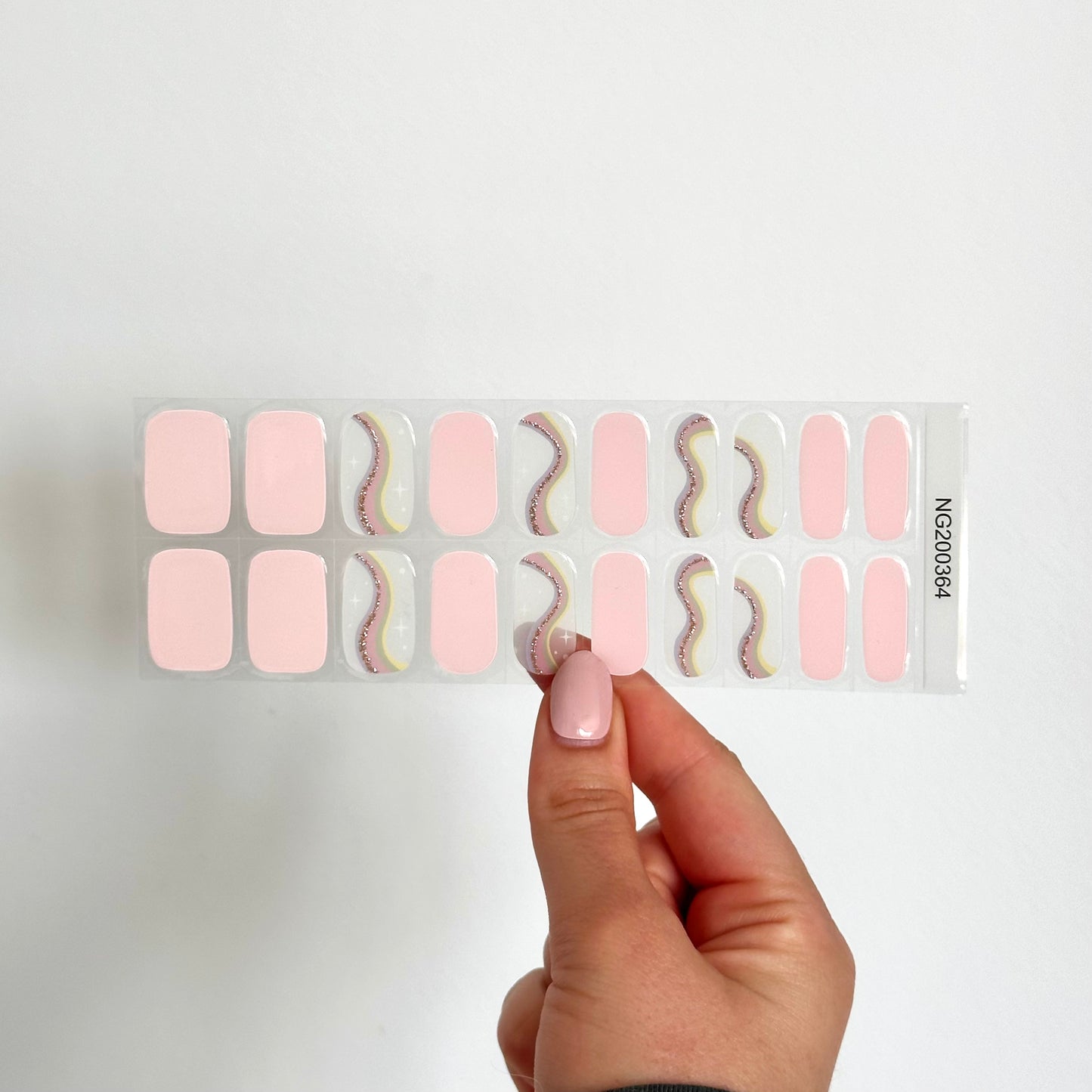 Gellakstickers met op een paar nagels effen roze en op andere nagels semi-transparante basis met zacht neutrale kleur regenboog en subtiele glitterboog