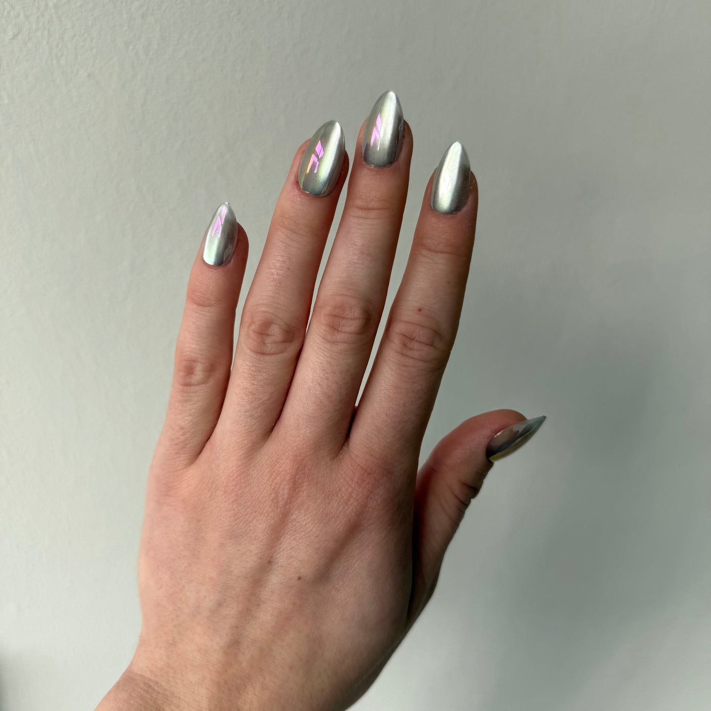 Een bijna spiegelende cat-eye chrome press-on nagel in almond vorm in een mooie zilveren kleur die in het licht roze, paarse reflecteert