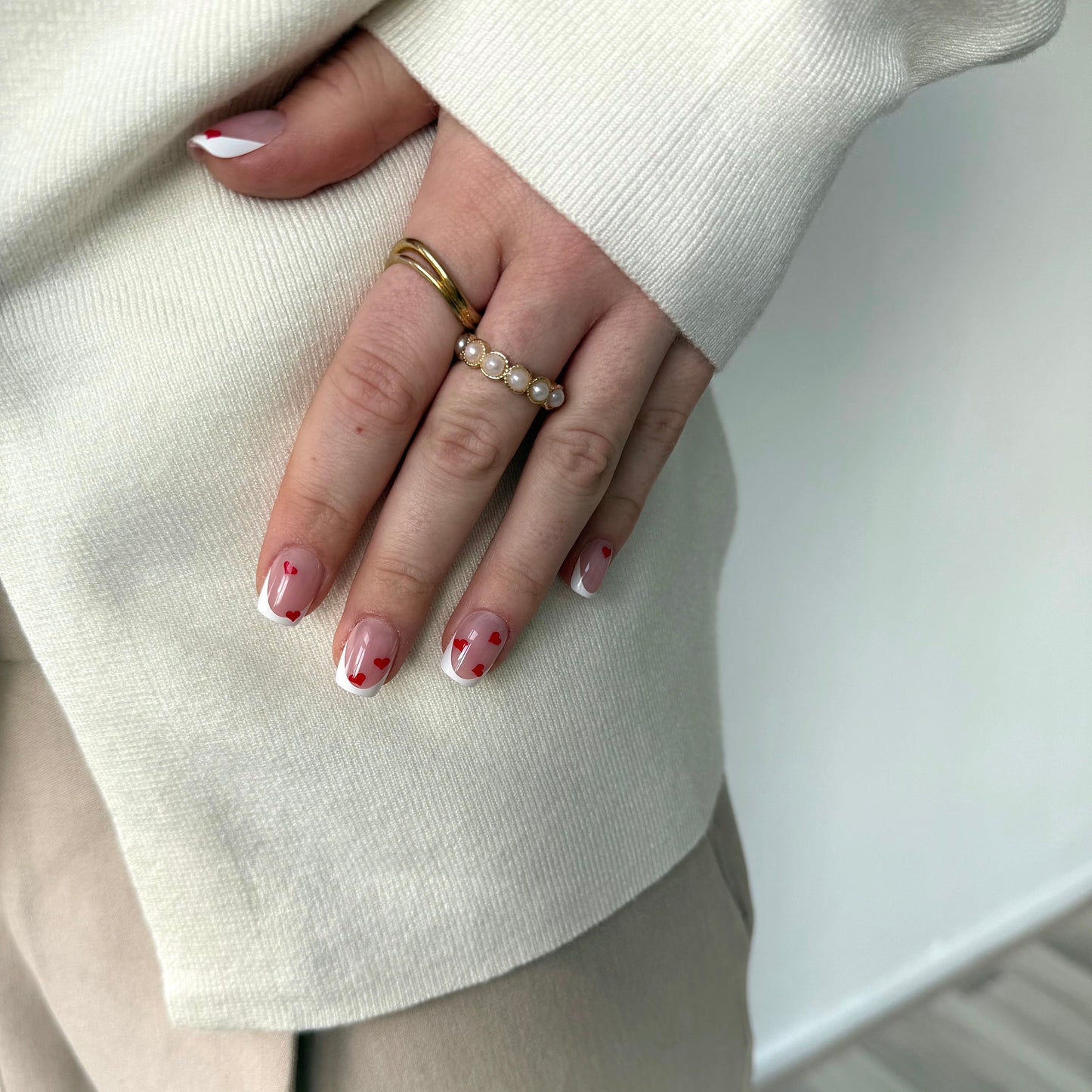 Lifestyle foto. Hand met ringen en press-on nagels van BIMA Nails. Een klassieke french manicure in square vorm met subtiele rode hartjes