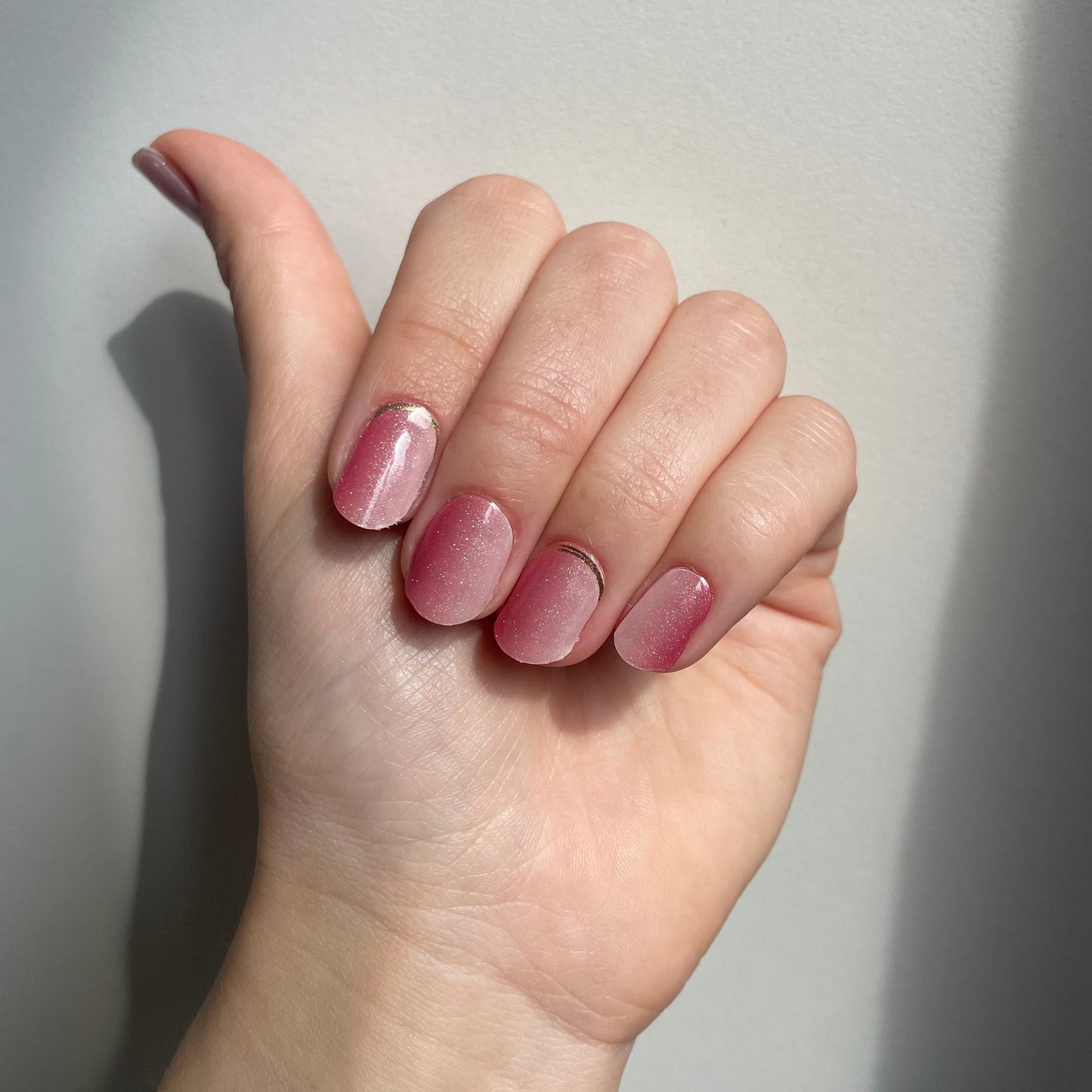 Een roze verticale ombre gellaksticker met glittertjes erdoorheen. Op sommige nagels zit aan de onderkant bij de nagelriem nog een gouden randje
