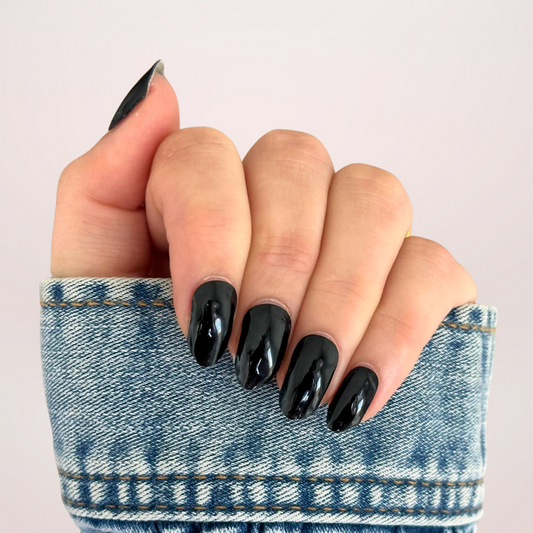 Close-up van een hand met effen zwarte gellakstickers op de nagels, die een intens diepe kleur en een strakke, glanzende afwerking tonen voor een stijlvolle en tijdloze look