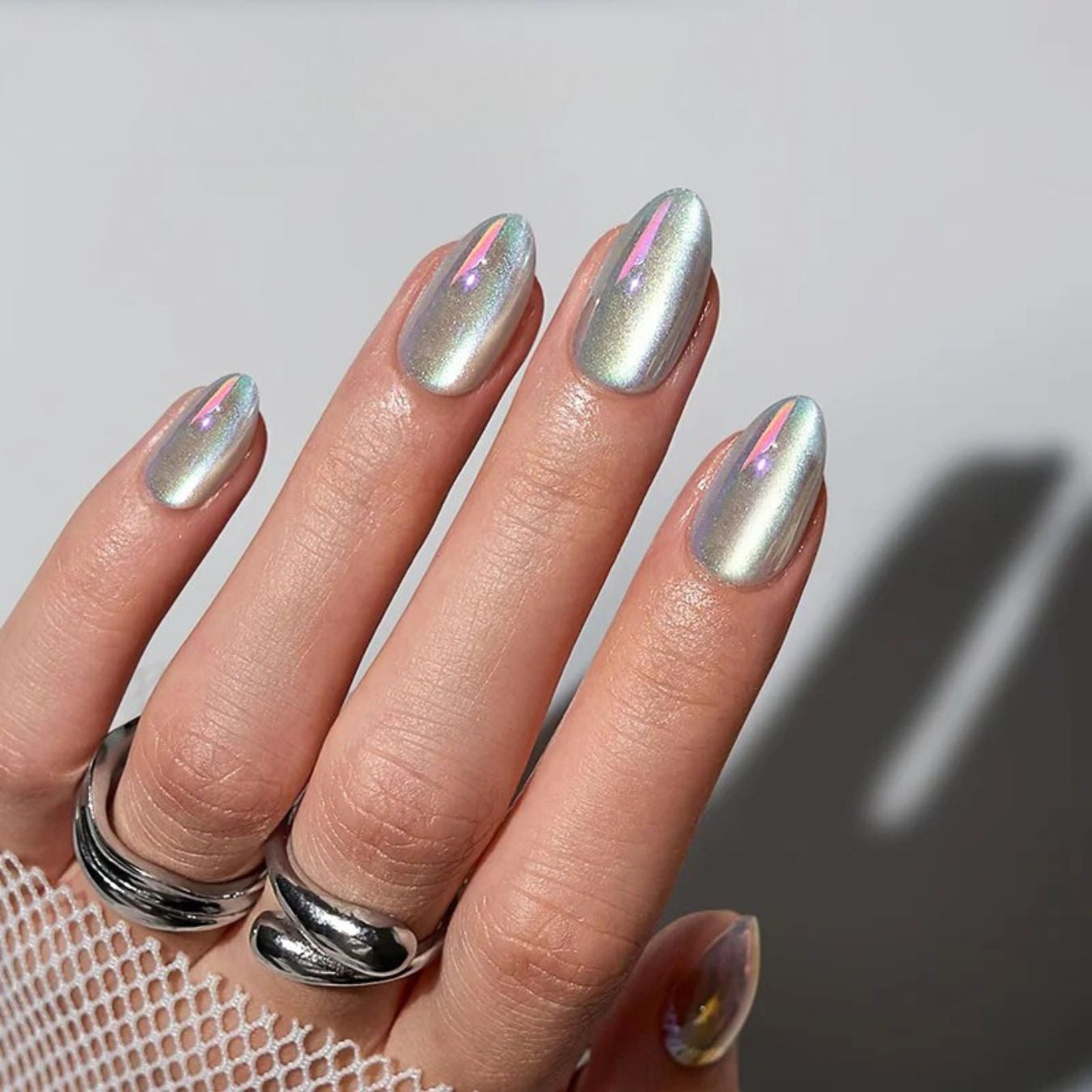 Een bijna spiegelende cat-eye chrome press-on nagel in almond vorm in een mooie zilveren kleur die in het licht roze, paarse reflecteert