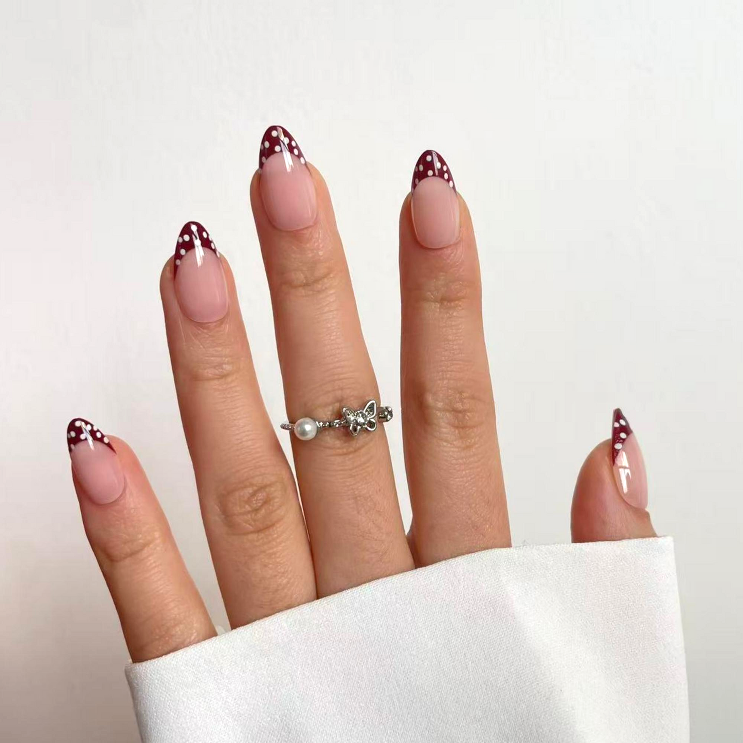 French manicure met twist. De tip is bordeaux rood, tegen het bruin aan en heeft polkadots. Verder is het volledig nude. Het is een almond vormige press-on