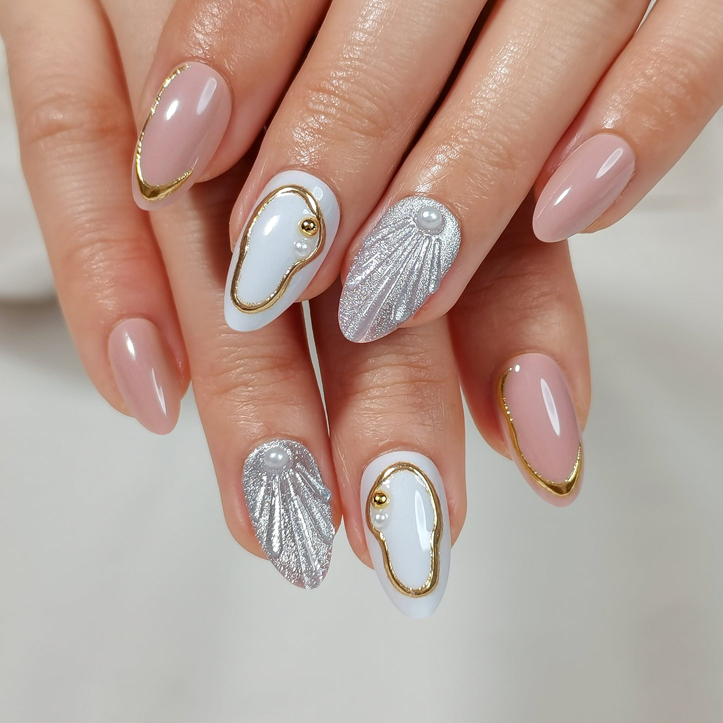 Luxe soft gel press-on nagels met gouden lijnen, pareldetails, schelpdesign en nude basis in almond vorm