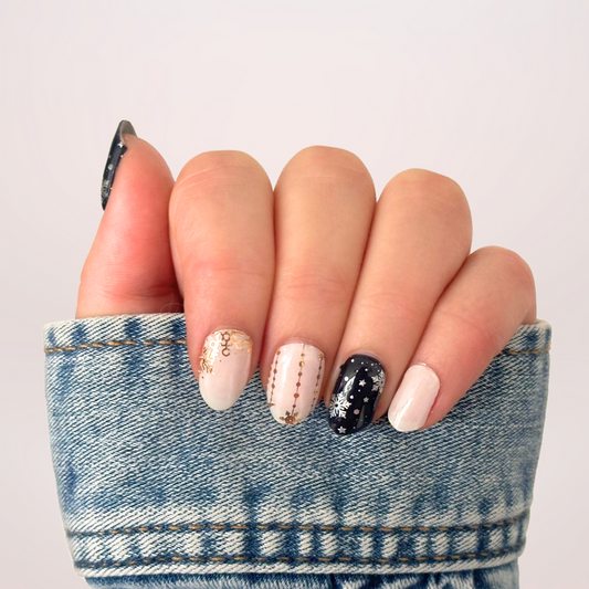 Winterse nail art. De ene nagel heeft een witte achtergrond met gouden details zoals kleine sneeuwvlokjes en maantjes, de andere nagel heeft als ondergrond donker blauw met witte sneeuwvlokken en sneeuw stippen. Perfect voor de winter